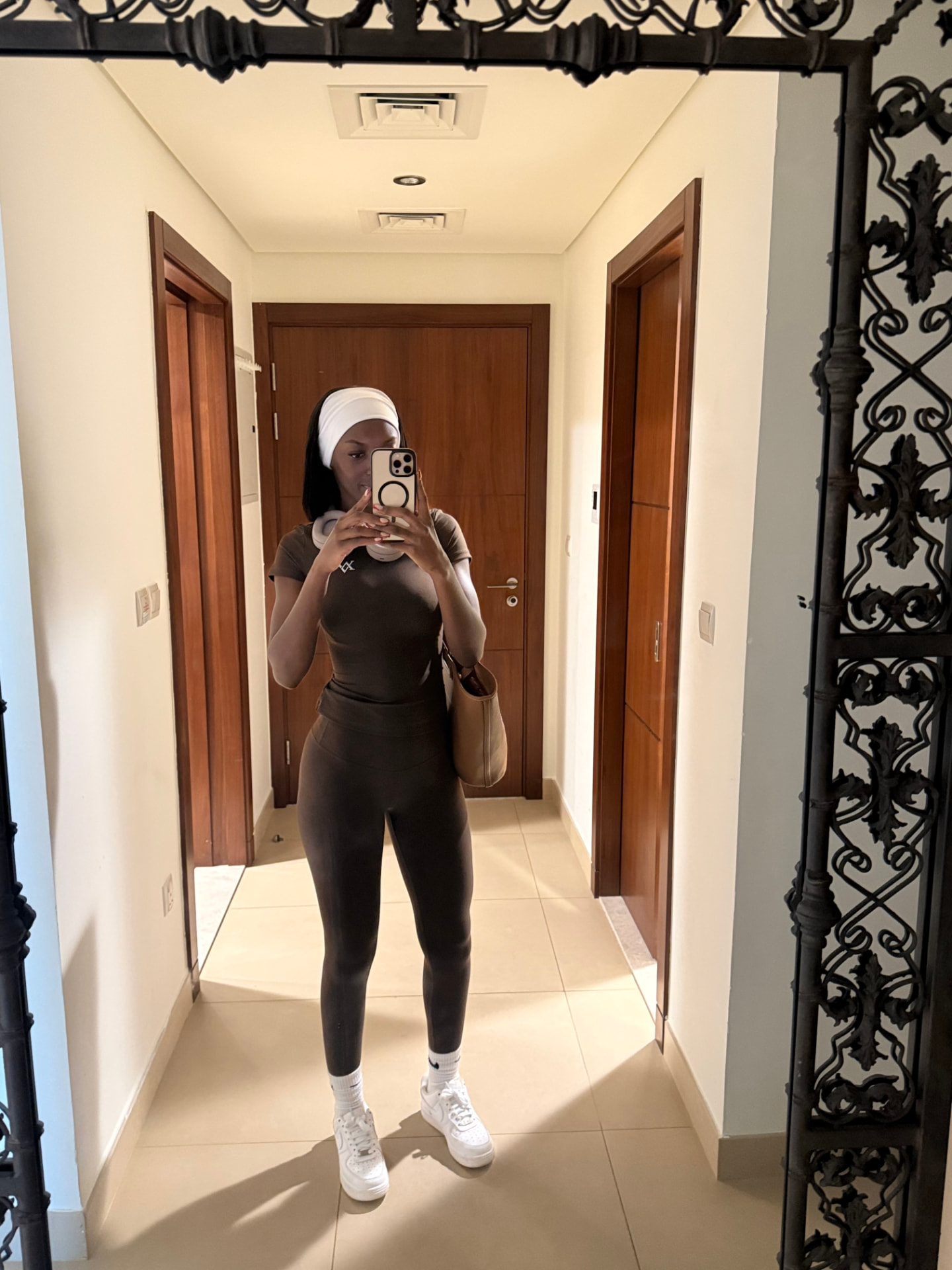 Woman in a brown Valentin Noble activewear set with a headband and tote bag in a sunlit hallway